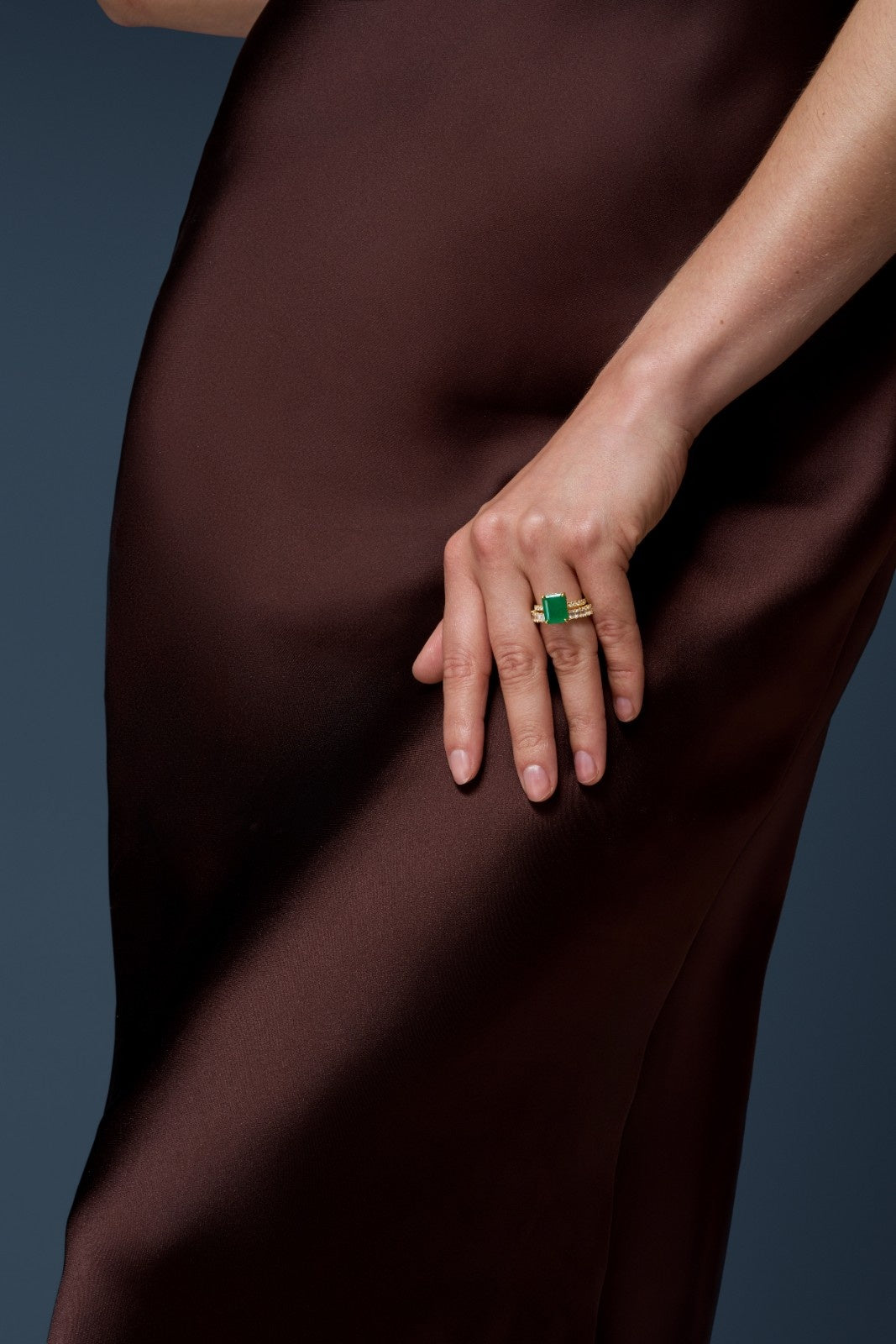 Hand wearing a green ring on a dark fabric background